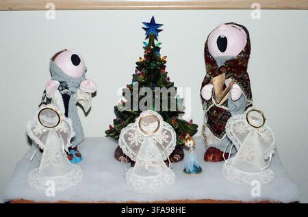 A whimsical holiday display featuring handmade folk art caroler figurines, lace angel ornaments, and a glowing ceramic Christmas tree with colorful li Stock Photo