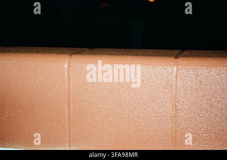 Close-up of wet red brick wall with glistening moisture on textured surface against dark night background. Moody and urban feel. Stock Photo