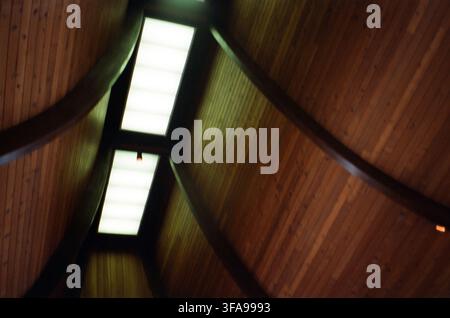Looking up at a warm wooden paneled ceiling with angular skylight windows allowing natural light in, creating dramatic geometric shadows and warm tone Stock Photo