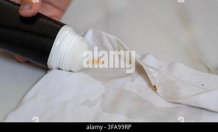 Close up of a hand applying liquid from a black tube onto white fabric with visible brown stains, showing a household cleaning or stain treatment proc Stock Photo