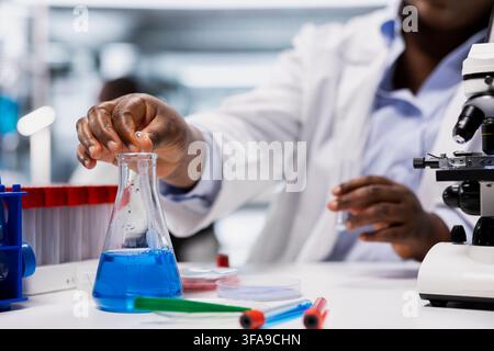Close up of laboratory specialist pipetting agent into blue test tube sample to improve chemical formulation. Analytical chemist observing reaction in test tube to verify scientific hypothesis Stock Photo