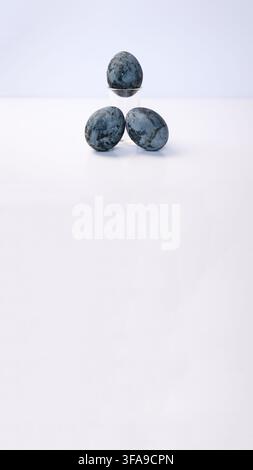 Three dark blue marbled Easter eggs styled on a clear glass stand against a seamless white background with copy space. Easter decor aesthetics, sacral Stock Photo