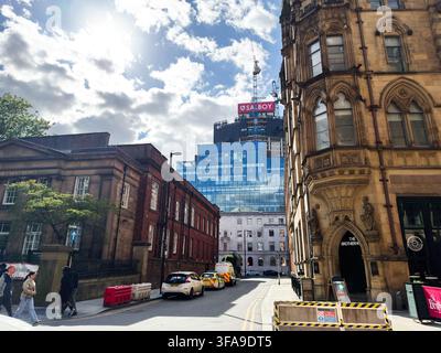 Manchester, UK - May 10, 2026: Historic and modern buildings line a sunny Manchester street with pedestrians, construction crane and dramatic clouds. Stock Photo