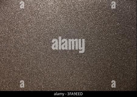 A detailed commercial close-up photograph of a dark, highly textured black abrasive sandpaper surface. The image highlights the sharp, granular grit particles embedded in the backing material, showing the coarse, functional texture used for sanding and polishing. Stock Photo