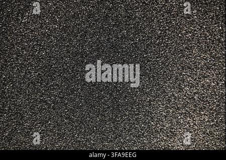 A detailed commercial close-up photograph of a dark, highly textured black abrasive sandpaper surface. The image highlights the sharp, granular grit particles embedded in the backing material, showing the coarse, functional texture used for sanding and polishing. Stock Photo