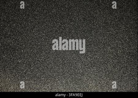 A detailed commercial close-up photograph of a dark, highly textured black abrasive sandpaper surface. The image highlights the sharp, granular grit particles embedded in the backing material, showing the coarse, functional texture used for sanding and polishing. Stock Photo
