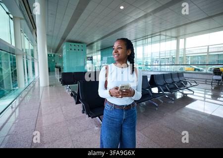 Young woman smiling, using smartphone in airport terminal. Stock Photo