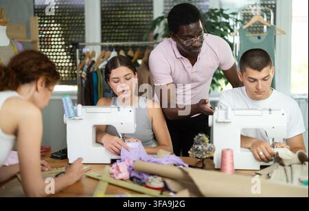 Middle-aged male teacher helping students sew while other drawing paper Stock Photo