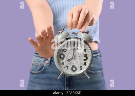 Time management and deadline pressure, woman holding an alarm clock with a stop gesture on a purple background Stock Photo