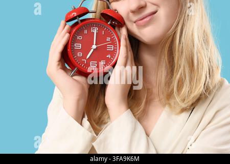 Time management and punctuality concept, young woman holding a red alarm clock with a happy expression on blue background Stock Photo