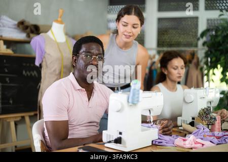 Middle-aged female teacher helping students sew Stock Photo