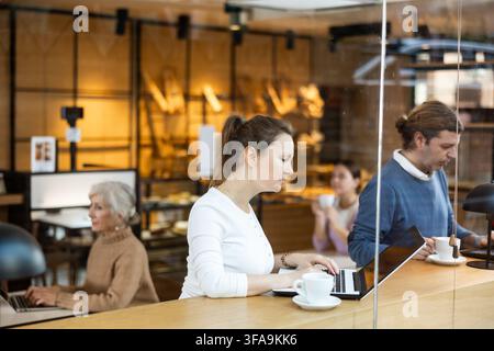 Focused woman drinking coffee while working on laptop in cozy cafe Stock Photo