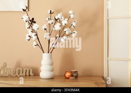 Cozy home decor and hygge lifestyle, cotton branches in a white vase with candles and a dream sign on a wooden shelf Stock Photo