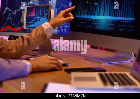 Financial data analysis and stock market trading, person pointing at computer screen with charts and graphs in a dark office Stock Photo