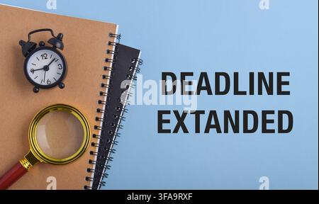 Deadline extended text with alarm clock, magnifying glass and notebooks on a blue background. Concept of deadline extension, project management Stock Photo