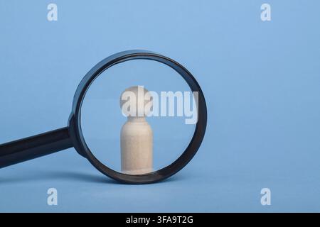 Wooden person figure highlighted through magnifying glass on blue background. Concept of customer identification, target audience, user profiling, rec Stock Photo