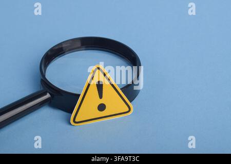 Magnifying glass and warning sign on blue background with copy space. Concept of risk assessment, hazard identification, danger detection, safety insp Stock Photo