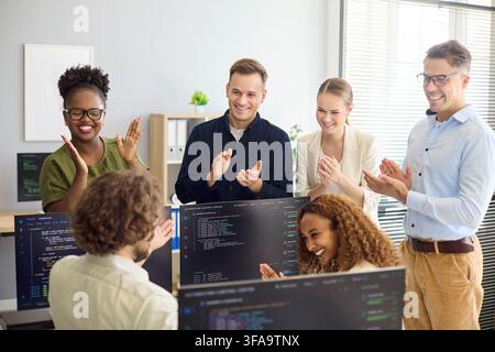Diverse developer team applauding successful code release in modern office meeting Stock Photo