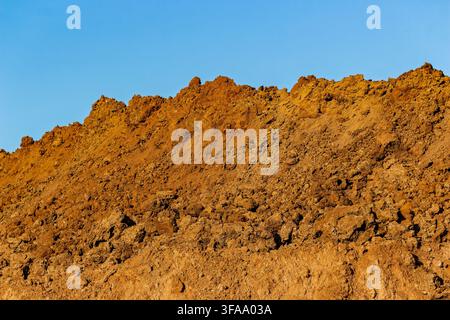 Large piles of excavated brown soil and dirt mounds from earthmoving construction works against a clear blue sky, capturing textured land layers and i Stock Photo