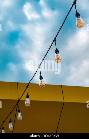 Decorative string lights hanging against a blue sky and yellow building wall. Stock Photo