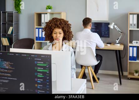Developers coding software in modern office with monitors and team collaboration Stock Photo