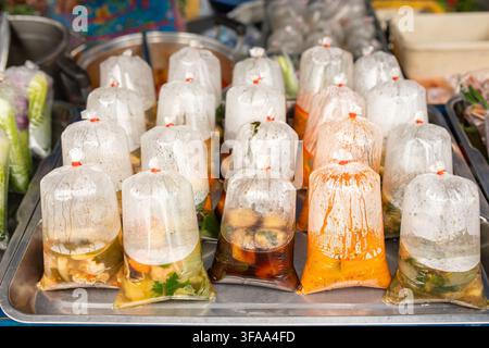 Variety of Thai street food soups packaged in clear plastic bags for takeaway, Asian street food vendor concept Stock Photo
