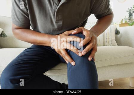 Man holding his knee while sitting on a couch Stock Photo