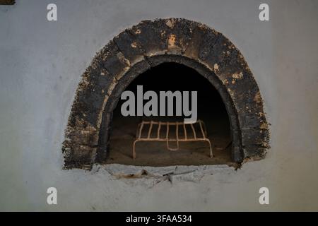 Old arched masonry oven set into a plastered wall, with darkened stonework and a rusted metal rack inside. Suitable for architecture and traditional i Stock Photo