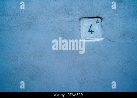 Small number four plaque embedded in a blue textured plaster wall, with a fine surface crack and generous empty space around the architectural detail. Stock Photo