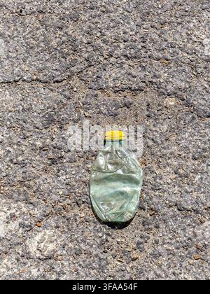 Mexico, 2026. A crushed discarded plastic bottle lies on rough asphalt, a stark image of single-use plastic waste, litter and the environmental impact Stock Photo