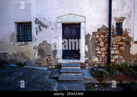Dark wooden door framed by carved stone in a weathered plaster facade with barred windows, exposed brickwork and worn masonry surfaces. Stock Photo