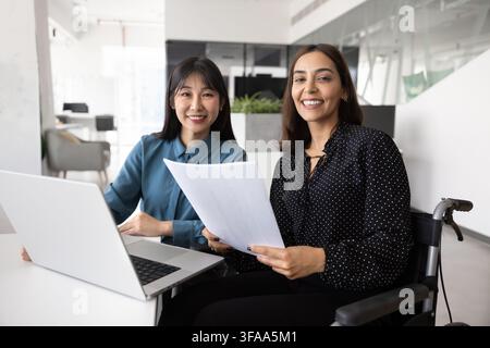 Woman with disability sits in wheelchair working together with colleague Stock Photo