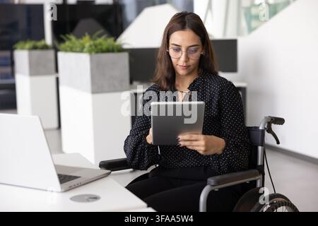 Focused professional woman in wheelchair using digital tablet Stock Photo