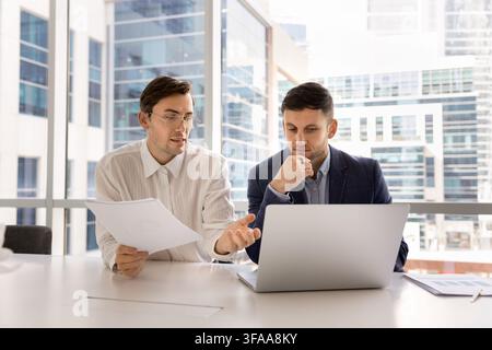 Business executives checking information on laptop and papers in office Stock Photo