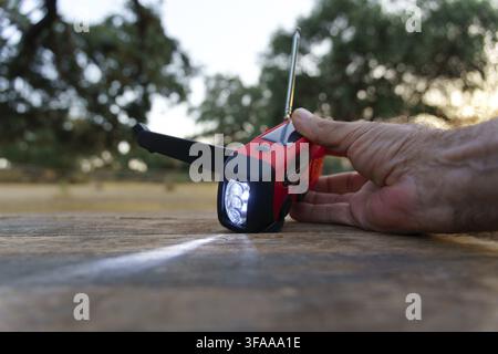 Ronda, malaga, spain Hand holding a red emergency crank radio with a flashlight beam on a rustic wooden table, useful for survival and outdoor activit Stock Photo