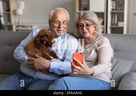 Senior couple video calling on smartphone with pet dog Stock Photo