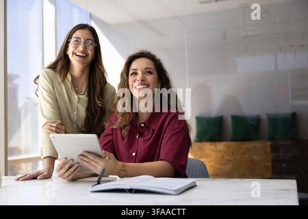 Smiling women colleagues engaging in business strategy planning, project review on digital tablet, laughing, posing for professional portrait, represe Stock Photo