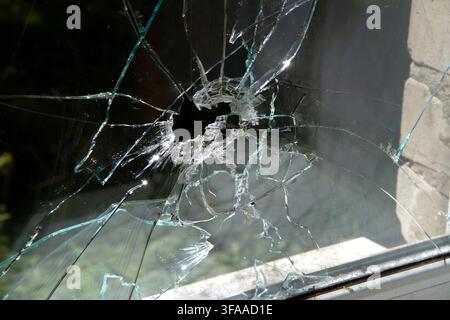 Window glass shattered by a shell fragment. Broken window glass close-up. Stock Photo