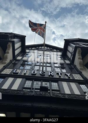 Low-angle view of the Tudor revival facade of Liberty London department store featuring the illuminated sign and Union Jack flag. London, UK. Stock Photo