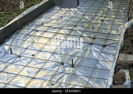 Workers pouring concrete onto a rebar grid and vapor barrier, creating a new foundation slab during a construction project Stock Photo