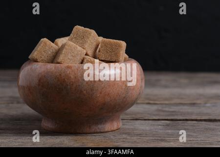 Brown cane sugar cubes packed in marble bowl standing on rustic dark wooden table surface Stock Photo