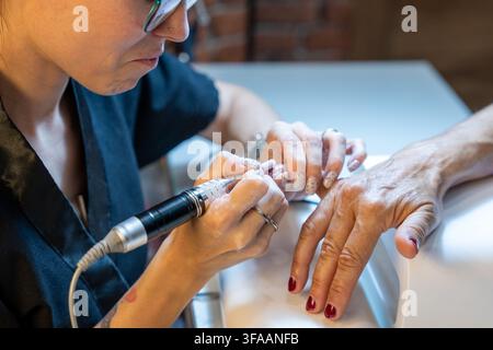 Nail technician performing a manicure on a client using an electric nail file Stock Photo