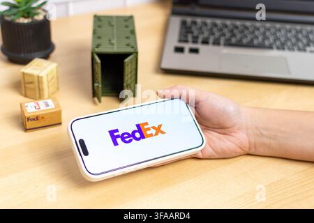 Hand holding an iPhone with the FedEx app logo. Stock Photo