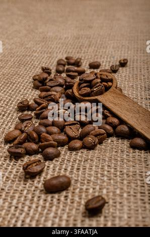 Roasted coffee beans with a wooden scoop on rustic burlap background Stock Photo