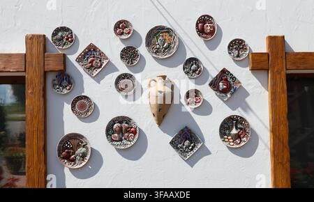 Traditional decorative ceramic plates and clay amphora hanging on white wall. Beautiful handmade pottery souvenirs featuring ethnic patterns and Stock Photo