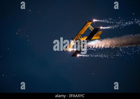 View of a yellow Grumman G-164 Ag-Cat biplane performing aerobatics with pyrotechnics and smoke trails during the Antidotum Airshow in Leszno, Greater Stock Photo