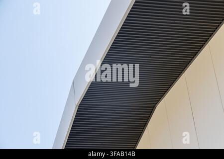 Abstract view of contemporary building facade featuring ribbed metal and textured panels under a clear sky Stock Photo