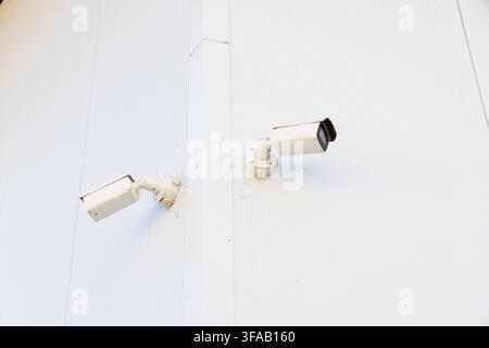 Outdoor security cameras are positioned on a ribbed white facade, suggesting a focus on property protection and surveillance Stock Photo