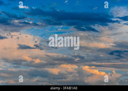 Stunning dramatic sky background featuring a mix of blue, grey, and golden orange cumulus and stratocumulus clouds illuminated by the soft light of su Stock Photo