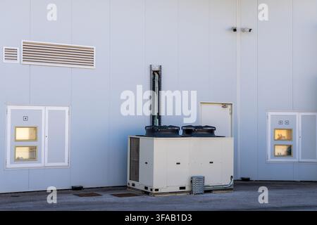 Large commercial air conditioning system with visible fans and ductwork mounted on the side of a corrugated metal building Stock Photo